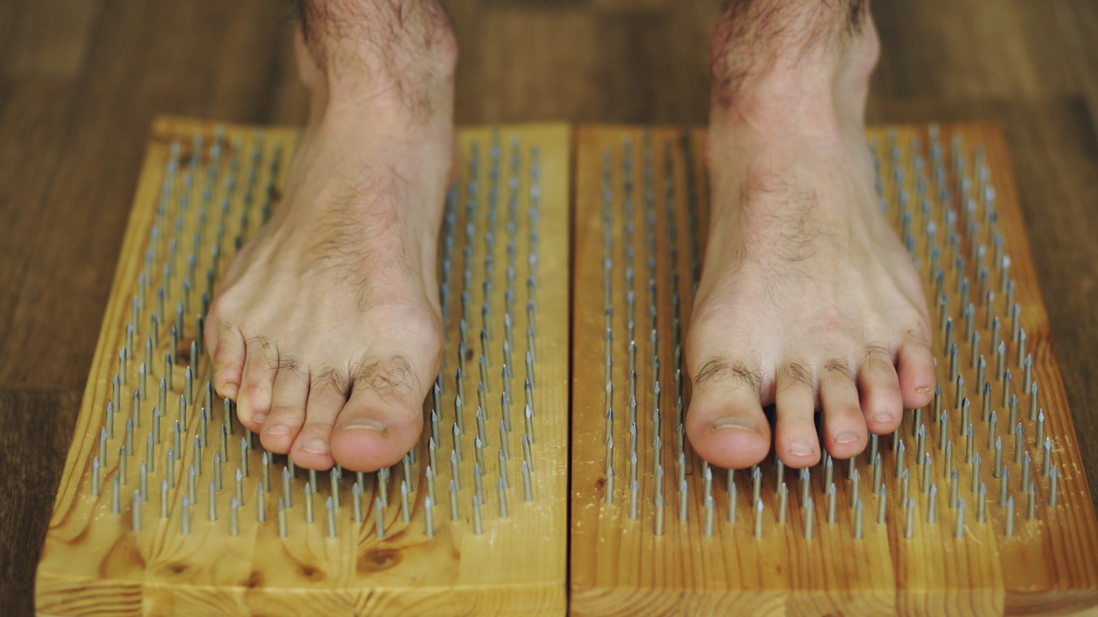 Bare feet standing on wooden boards with nails.